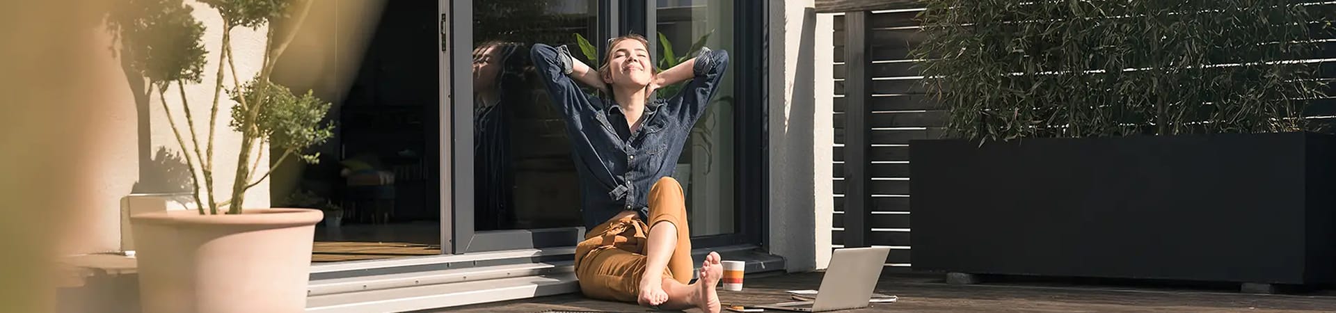 Frau entspannt auf der Terrasse vor großen Fenstern mit Sonnenschutz – modernes Wohnen mit LAKAL Lösungen.
